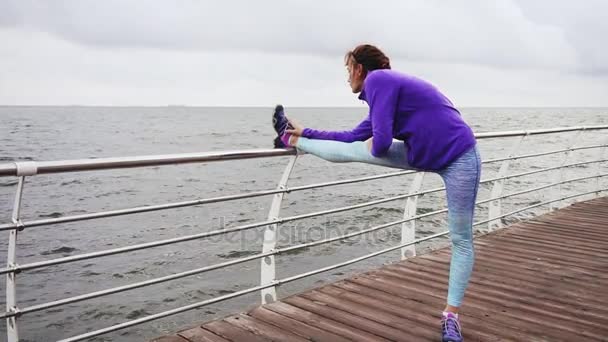 Mujer atlética estirando las piernas antes de trotar en la playa junto al mar temprano en la mañana. Entrenamiento junto a la playa en verano — Vídeo de stock