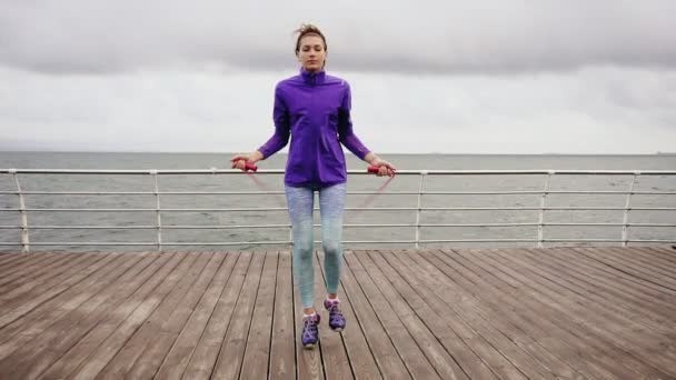 Young athtletic woman working out on the jump rope. Slim girl jumping on a skipping rope by the sea. Slowmotion shot — Stock Video