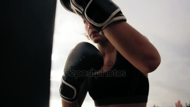 Vista de perto de um boxeador feminino atlético forte em luvas que se exercitam com uma bolsa. Treino lá fora. Treino de pugilista feminino. Conceito de autodefesa. Tiro em câmara lenta — Vídeo de Stock