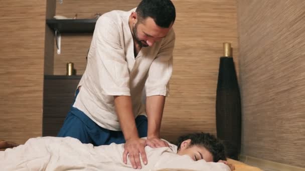 Massagista tailandês masculino está tratando mulheres jovens para trás e ombro. Sessão de massagem tailandesa para jovem mulher atraente em quimono. Tiros em 4K — Vídeo de Stock