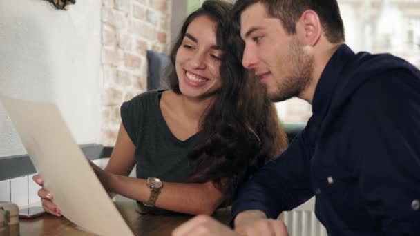 Jeune couple mignon regardant le menu et choisissant ce qu'il faut commander pour le déjeuner. Tourné en 4k — Video