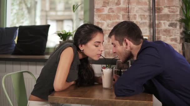 有吸引力的年轻夫妇，在咖啡馆里坐在木桌和喝奶昔用吸管。幸福的夫妇在假期放松在咖啡馆 — 图库视频影像