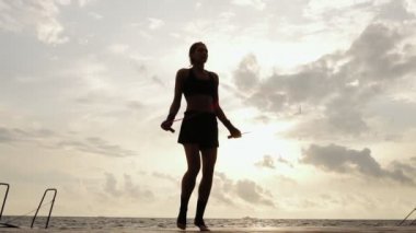 Tanınmayan atletik kadın slowmotion Beach'te güneşin karşı ip atlama üzerinde çalışma dışarı. Kız deniz kenarında bir atlama ip atlama