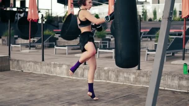 Video ad alto ritmo: Forte pugile atletica in guanti che si allena con una borsa. Colpisce una borsa con la gamba. Allenati fuori. Allenamento femminile di pugile. Colpo di rallentamento — Video Stock