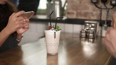 Kiraz üstünde belgili tanımlık tepe ve saman telefonlarını kullanarak Cafe ahşap bir masa üzerinde erkek ve kadın bir bardak süt ile fotoğraflarını el sallamak