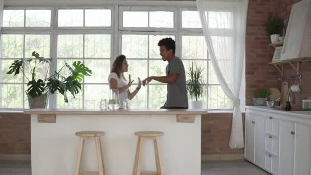 朝のパジャマを着てキッチンで音楽を聴いてダンス家幸せな若いカップル。家庭で楽しい恋の multiethnical カップル。スローモーション撮影 — ストック動画