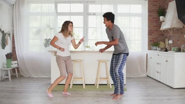 Feliz pareja multiétnica bailando en la cocina en pijama. Atractiva pareja enamorada divirtiéndose en casa. Disparo en cámara lenta — Vídeos de Stock