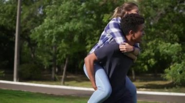Mutlu bir çok ırklı çift romantik Tarih: beyaz mutlu kız piggybacking ve onu güneşli parkta yeşil çimenlerin üzerinde koşturup iplik Afrika yakışıklı