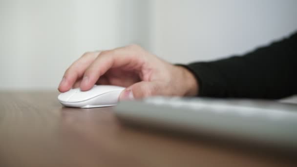 Vista lateral de una mano de hombre joven usando el ratón de computadora inalámbrico sentado en la mesa de la oficina. Mesa de escritorio de madera. Disparo en 4k — Vídeo de stock