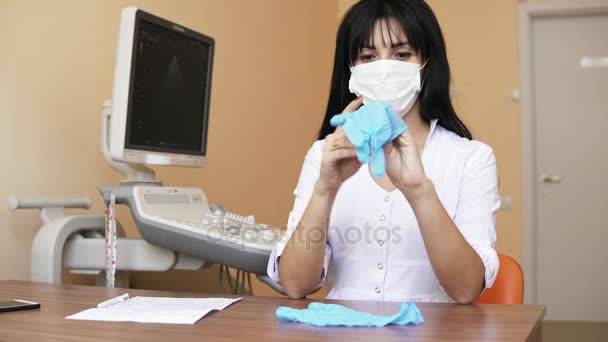 Ärztin legt sterile Handschuhe an, während sie in ihrem Büro am Tisch sitzt und sich auf die Operation vorbereitet. Schuss in 4k — Stockvideo
