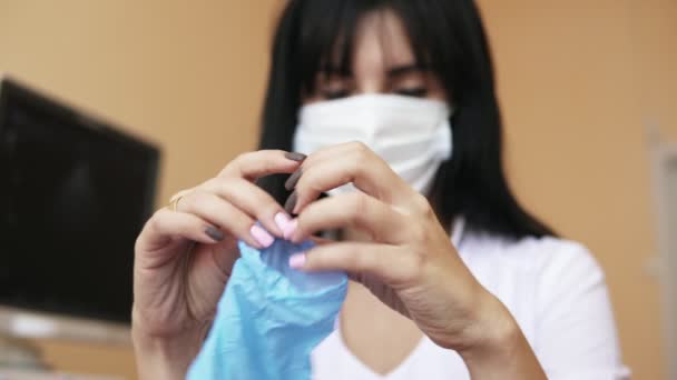 Närbild bild av kvinnliga läkare händer bär latexhandskar. Oigenkännlig sjuksköterska i kirurgisk mask dressing medicinska handskar när du sitter vid bordet på hennes kontor. Sköt i 4k — Stockvideo