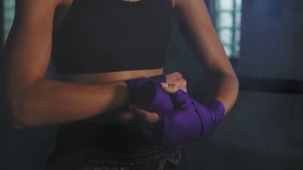 Vue rapprochée du boxeur féminin muay thai enveloppant des bandages sur ses mains avant de se battre dans une pièce sombre avec de la fumée. Tourné en 4k — Video