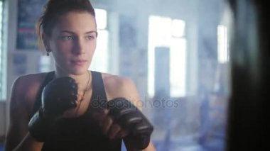 Onun elinde eldiven duman ile spor salonunda boks çantayla isabet beyaz kadın boksör closeup görünümü. Bir kadın kick boks sert güç eğitim