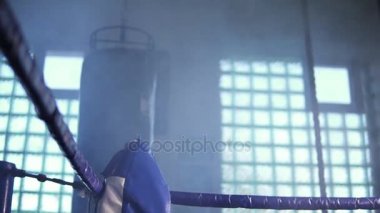 Dumanlı karanlık spor salonunda Boks ringi köşesine doğru geliyor ve kollarını yüzükteki ile dinlenme genç yorgun kadın boksör ipleri. Slowmotion atış