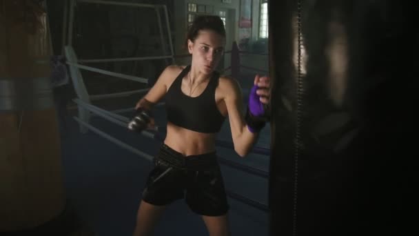 体育女拳击手在手套雷同拳击袋用她的拳头在烟雾弥漫的黑暗健身工作室训练时。慢动作镜头 — 图库视频影像