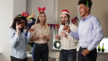 Gözlük köpüklü şarap ile tutarak ve prangalara Noel şapka ve geyik kafa bandı, kurumsal yeni yıl partisi sırasında dans mutlu ofis çalışanları çok ırklı grup