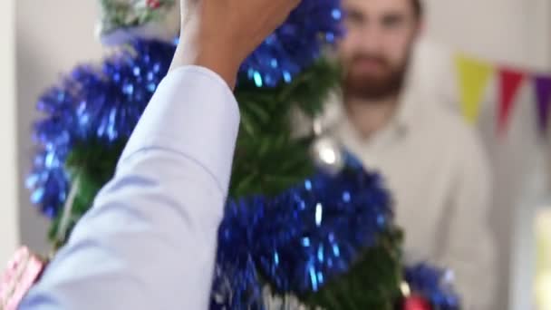 Крупним планом афроамериканська рука наносить прикрасу на вершину маленької штучної ялинки, прикрашеної офісними працівниками. Святкування Різдва в офісі — стокове відео