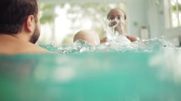 Cute baby having swimming lesson with his mother and father. Healthy family teaching their baby to swim in the swimming pool. Young father takes his son and embraces him while the kid is smiling — Stock Video