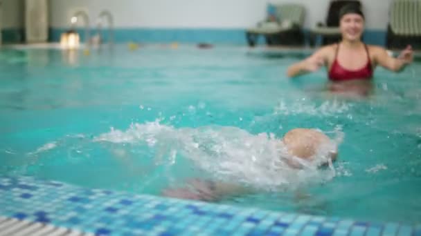 Jonge moeder vertoont naar haar zoontje om te duiken onder water in het zwembad, terwijl hij op de grens zit. Hij is springen, zwemmen, dan zijn vader is hem omhoog uit het water tillen — Stockvideo