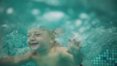 Sevimli sarışın yürümeye başlayan çocuk yüzme havuzunda su altında atlama ve annesi onu denizden kaldırma kadar orada yüzme. Bir sualtı çekim