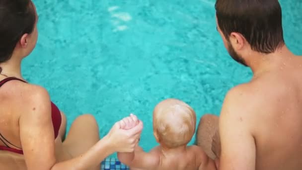 Vista posterior de la joven madre y el padre junto con su hijo saltando en la piscina cogidos de la mano. Madre y padre están enseñando a sus hijos a nadar. — Vídeos de Stock