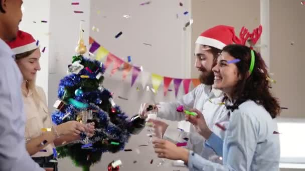 Jonge Afrikaanse kantoormedewerker squibs gewoon met confetti terwijl groep jongeren is het vieren van Kerstmis en Nieuwjaar in het kantoor mousserende wijn drinken uit glazen. Tikje schot — Stockvideo