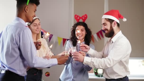 Group of young people toasting for achievements in New Year wearing christmas hats and deer antler headband and holding Bengal lights. Slowmotion shot — Stock Video