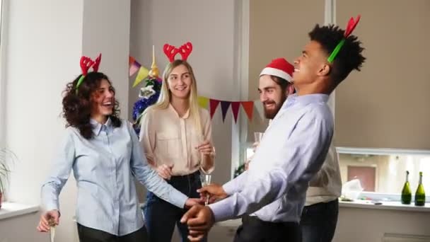 Plezier tijdens corporate Nieuwjaars party in het Bureau: multiraciale groep gelukkig kantoorpersoneel dansen tijdens corporate Nieuwjaar die het dragen van santa hoeden, houder is van bril met schuimwijn — Stockvideo