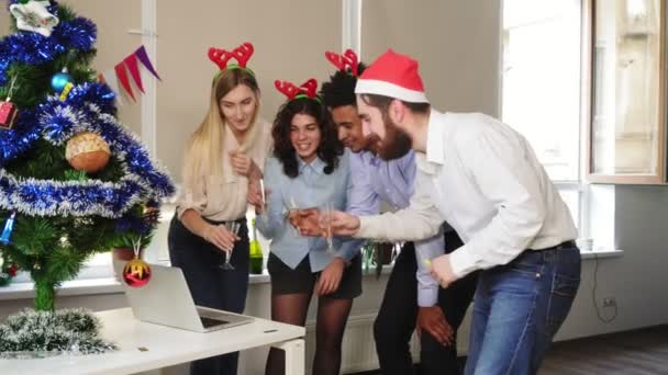 Вид сбоку на счастливую команду в шляпах Санта-Клауса, делающую конференц-звонок и звенящие бокалы с игристым вином на корпоративной вечеринке. Корпоративная новогодняя вечеринка в офисе. Международная команда — стоковое видео