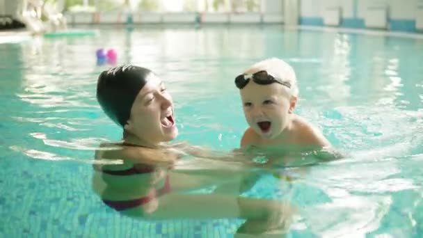 Feliz niño está nadando en la piscina junto con su madre. Ella lo sostiene y enseña a nadar. Feliz familia pasando tiempo juntos — Vídeo de stock