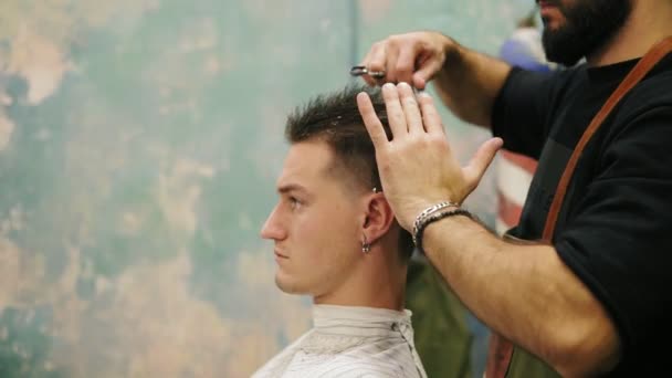 Side view of young handsome caucasian man with piercing in his ear getting his hair blow dried in a retro stylish barber shop — Stock Video