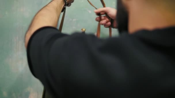 Junger stylischer Friseur bereitet sich auf einen Haarschnitt vor: Er zieht seine Lederschürze an und bindet Schürzenschnüre, bevor er mit der Arbeit beginnt — Stockvideo