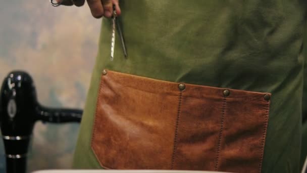 Крупный план мужских рук парикмахеров, помещающих заколки или заколки в карман в фартуке во время подготовки к стрижке. Инструменты для прически — стоковое видео