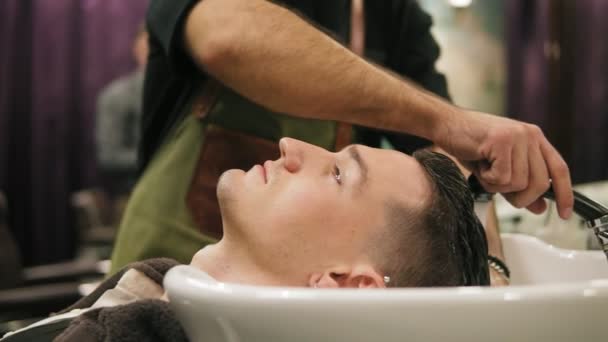 Крупным планом молодой человек моет голову неузнаваемым парикмахером в парикмахерской — стоковое видео