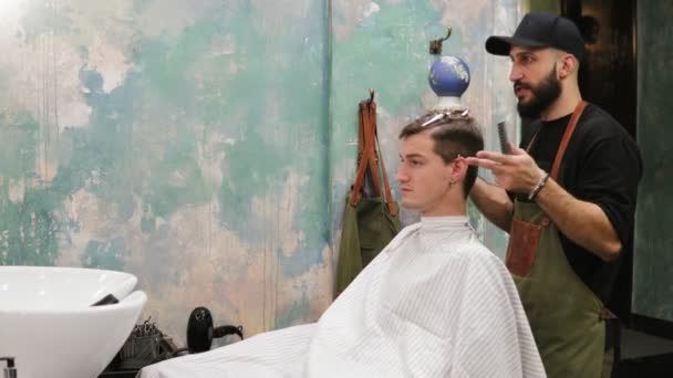 Porträt eines erwachsenen Mannes, der sich von einem bärtigen Friseur die Haare schneiden lässt, der gerade Haare schneidet — Stockvideo