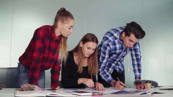 Группа дизайнеров интерьеров работает вместе в офисе. Молодые хипстеры делают наброски стоя за столом и обсуждают свой новый проект. Слоумоушн — стоковое видео