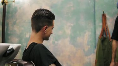 Onun kulak delici ile şık istemci ise sandalye etrafında dönerek Kuaför genç sakallı ve dövme orada oturuyor. Memnun müşteri çalışma sonucu gösterilen