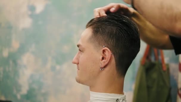 Vista de cerca de las manos de los peluqueros aplicando cera en el cabello de un cliente masculino con estilo en una barbería. Corte de pelo profesional para el joven hipster — Vídeo de stock