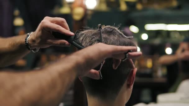 Slowmotion shot: Closeup view of the barbers hands performing a haircut with scissors and combing the client — Stock Video