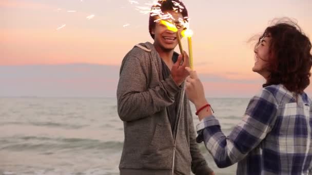 多民族カップル持株を笑って陽気な海のそばに立って日没時にキャンドル スパーク リング燃焼 — ストック動画