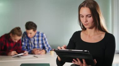 Çekici bir genç kadın ofiste ayakta ve iş arkadaşları bulanık arka plan üzerinde çalışırken onun tablet kullanma. Slowmotion atış