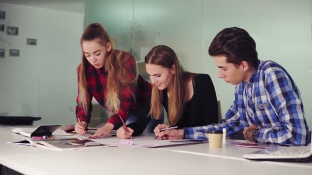 Группа молодых хипстеров, работающих вместе в современном офисе. Молодые профессионалы делают наброски сидя за столом, готовят свой новый проект и пьют кофе в медленном темпе — стоковое видео