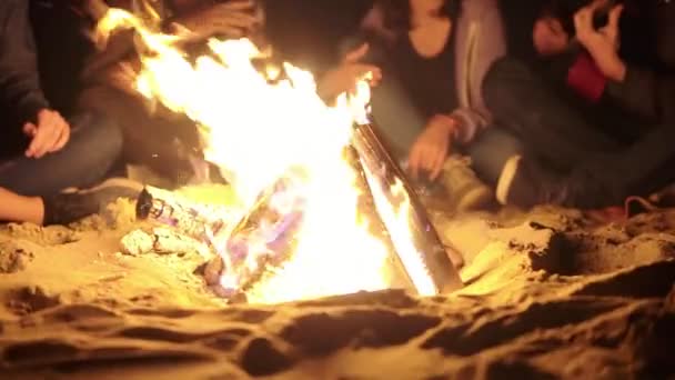 Closeup view of the bonfire late at night. Young people sitting by the fire in the evening. Cheerful friends singing songs and playing guitar, talking and having fun together — Stock Video