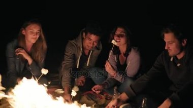 Gece geç saatte sahilde şömine başında oturan genç neşeli arkadaşları üzerinde hatmi kavurma ateşte birlikte sopa