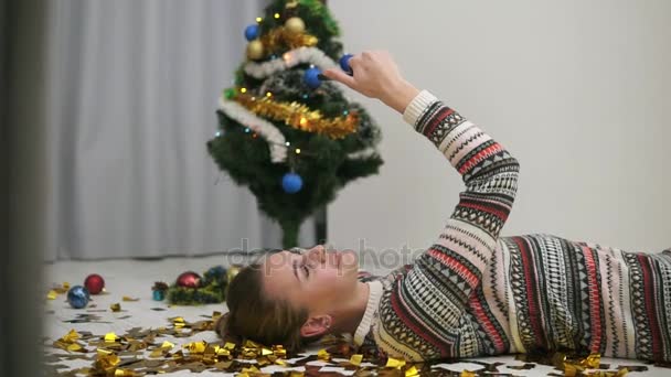 Bonne fille festive couchée sur le sol en confettis de paillettes d'or et de prendre selfie. Arbre de Noël décoré sur le fond — Video