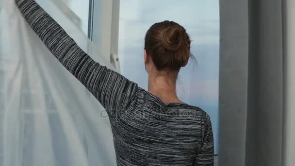 Silueta mladá žena blíží k odhalení záclonu a při pohledu z okna. Užívat si výhledu vně. Slowmotion shot — Stock video