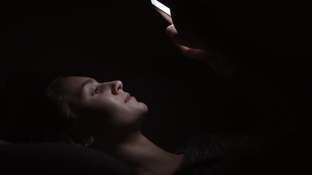 Nahaufnahme einer Frau, die auf einer Couch liegt und ihr Telefon in einem dunklen Raum benutzt, in der Dunkelheit mit dem Smartphone chattet, mit Freunden online kommuniziert — Stockvideo