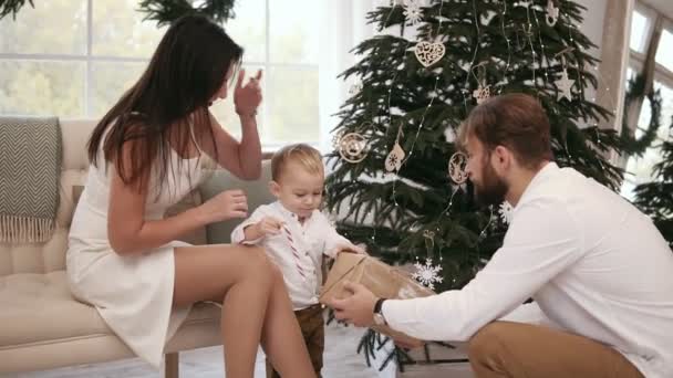 Blondes niedliches Kleinkind, das von seinem Vater ein Weihnachtsgeschenk bekommt. schönen Weihnachtsbaum auf dem Hintergrund. Familienweihnachtsfeier zu Hause — Stockvideo