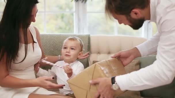 Blonde cute toddler receiving christmas present from his father. But he asks his mother to take him on her hands. Family christmas party at home — Stock Video