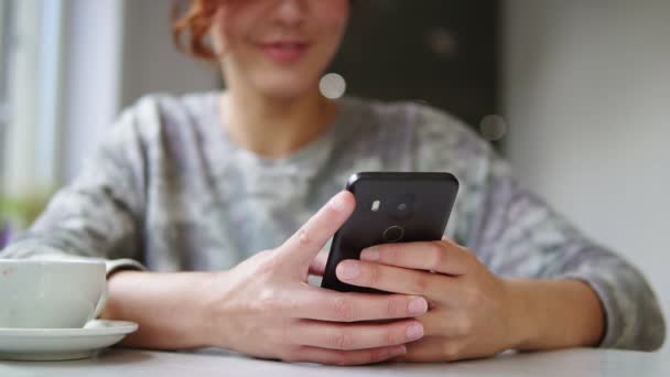 Mulher bonita usando seu telefone celular no café. e sorrindo. Mulher usando aplicativo no smartphone no café beber café e mensagens de texto no telefone móvel — Vídeo de Stock